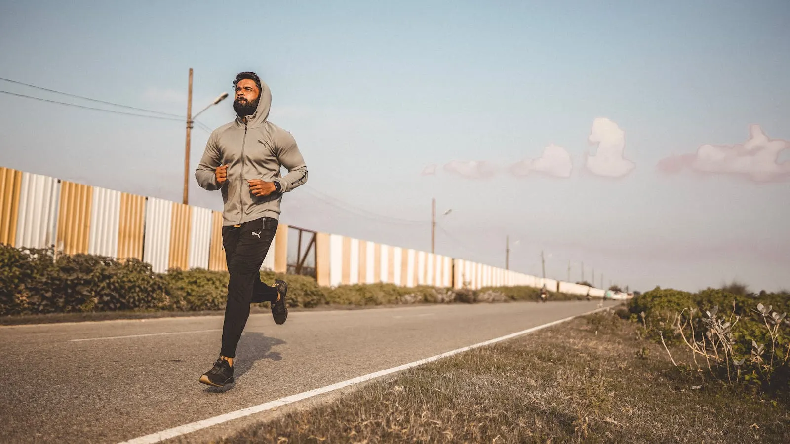 Man in a hooded sweatshirt running on an empty road under a blue sky