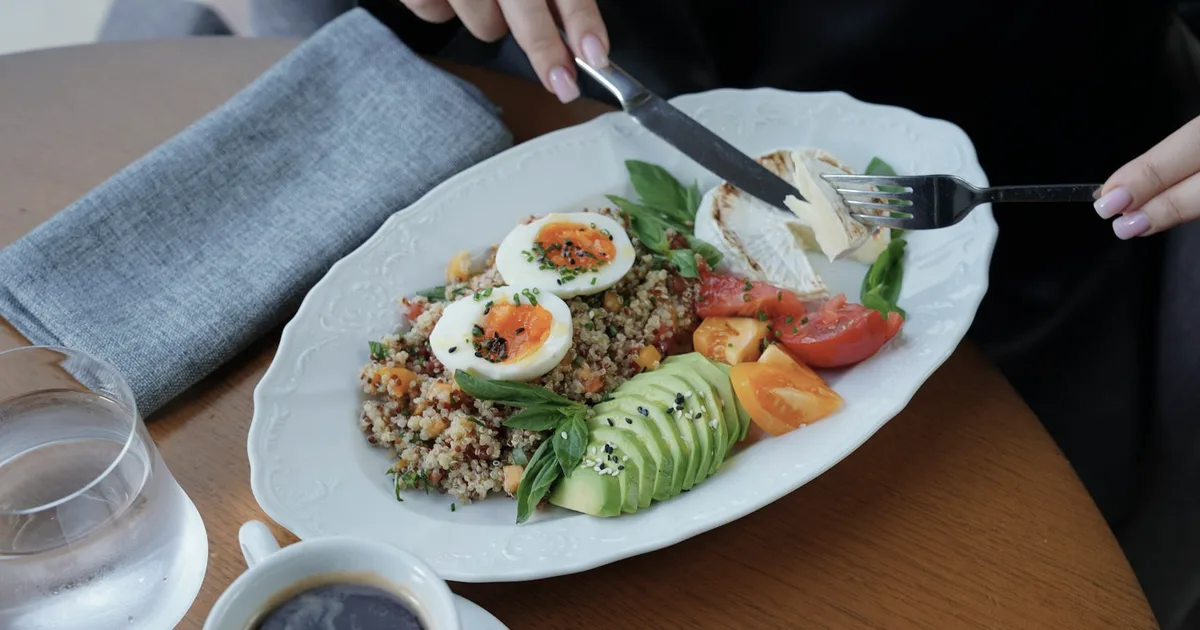 A balanced breakfast plate with eggs, avocado and coffee on a wooden table