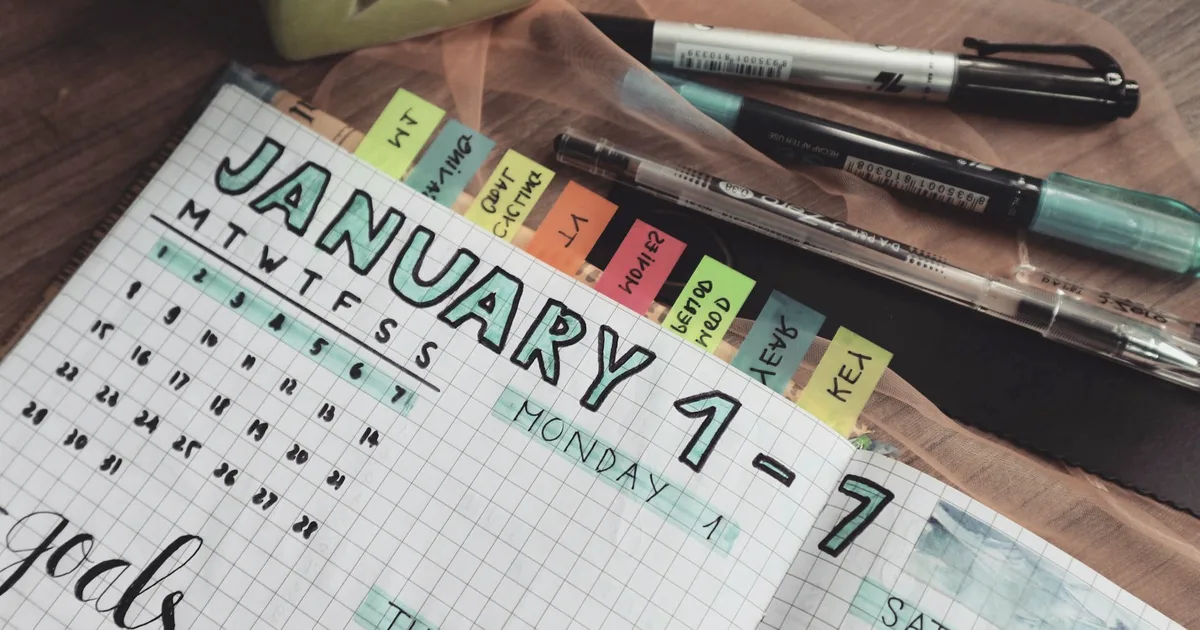 Agenda hebdomadaire papier avec onglets de couleur et stylos sur un bureau en bois