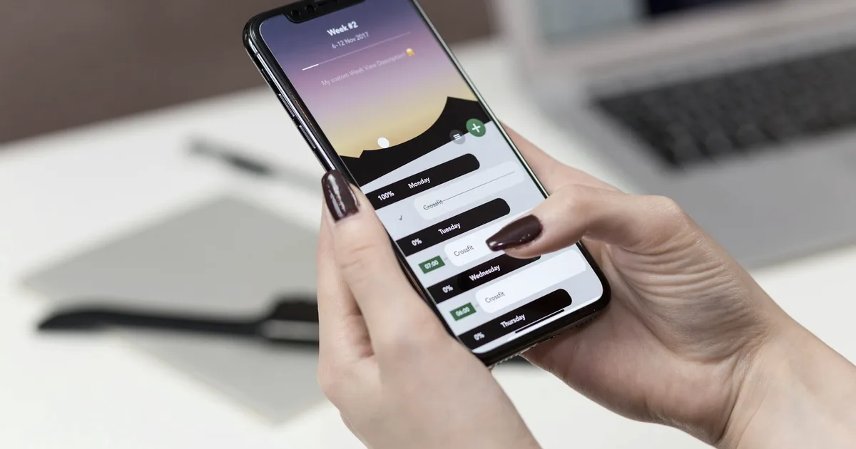 Main tenant un smartphone qui affiche une application de planification de la semaine