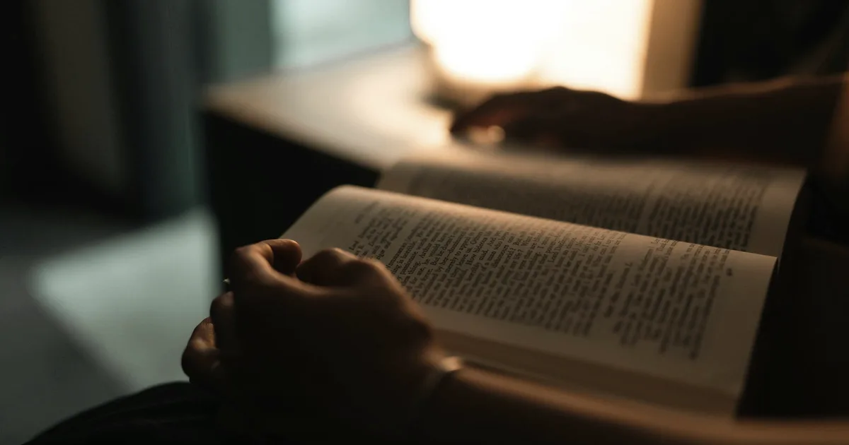 Personne en train de lire un livre à la lumière chaude d'une lampe, dans une ambiance calme de soirée