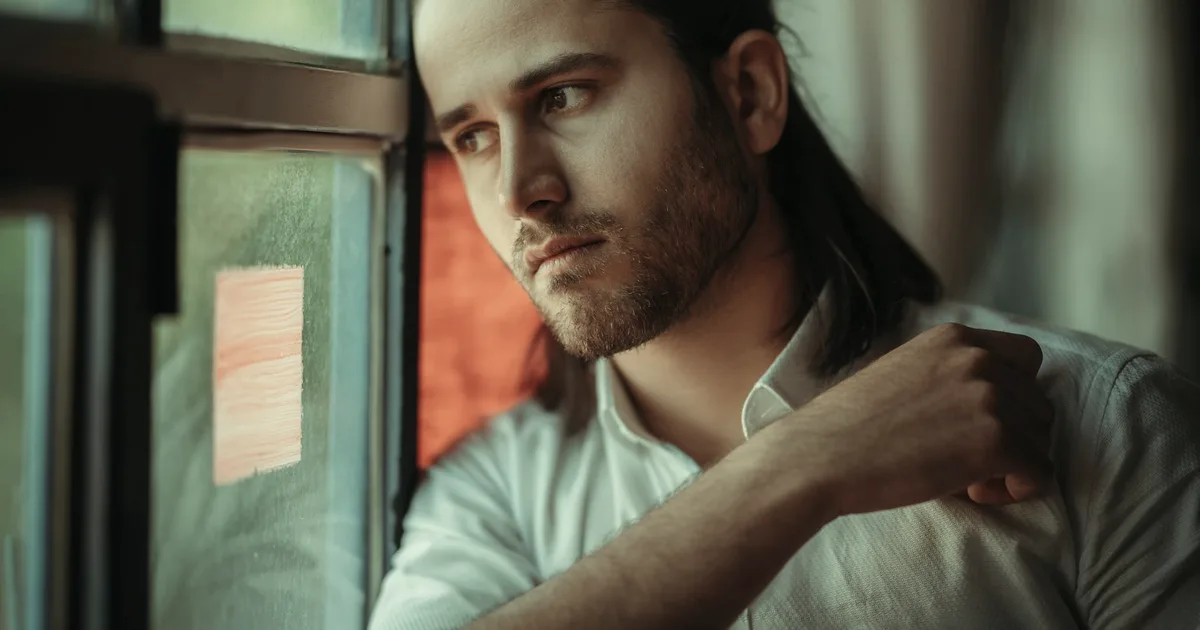 Man with an intense, alert gaze leaning against a window