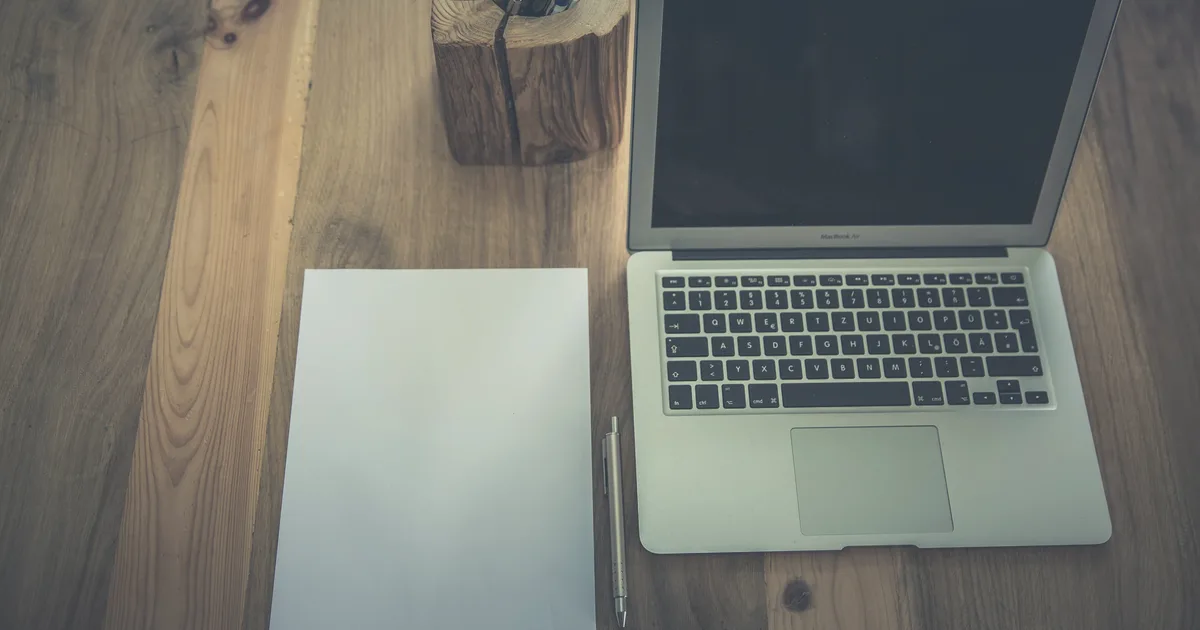 Bureau en bois avec ordinateur portable ouvert, carnet vierge et stylo, dans une lumière douce