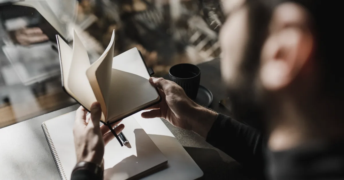 Person sitting by a window leafing through a notebook