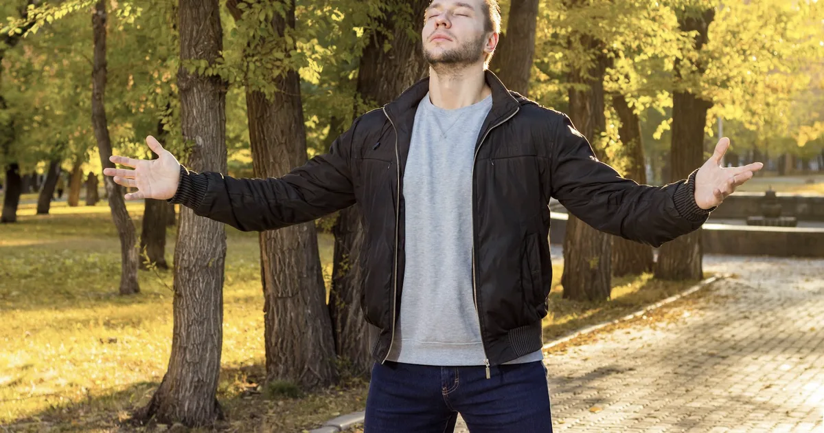A man with his eyes closed in a park bathed in golden light