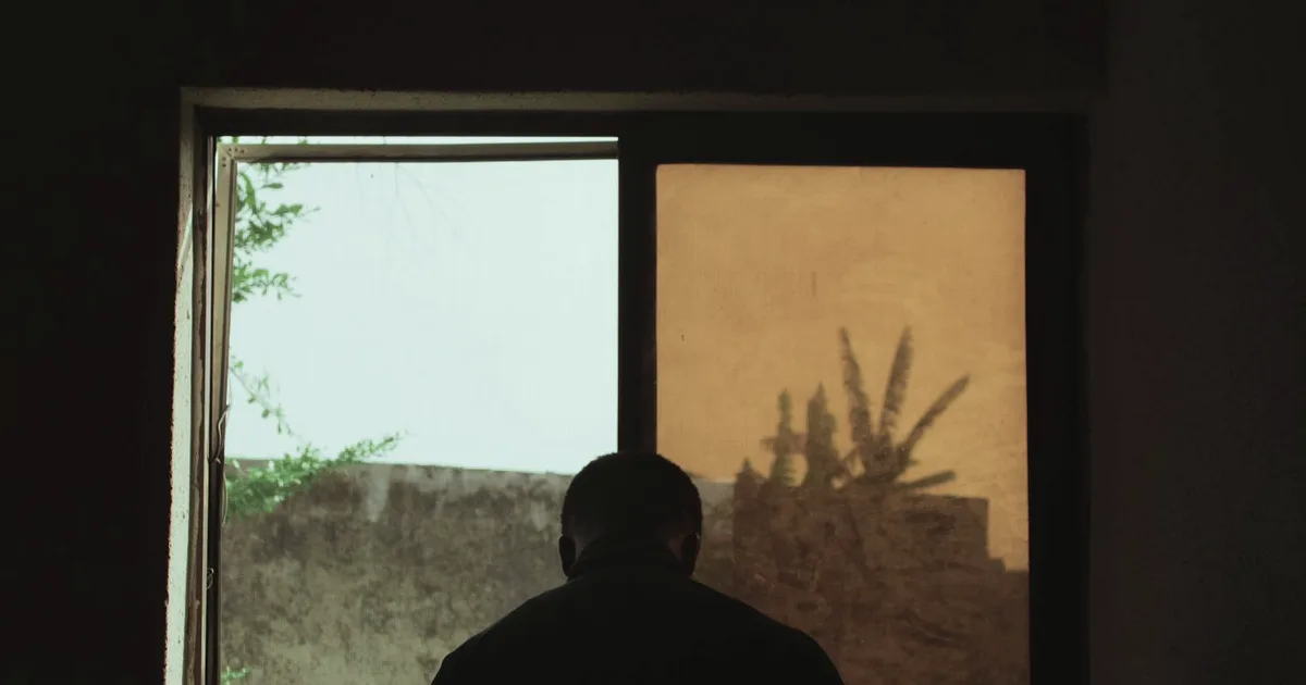 Silhouette of a man standing at a window in a dark room lit by warm light