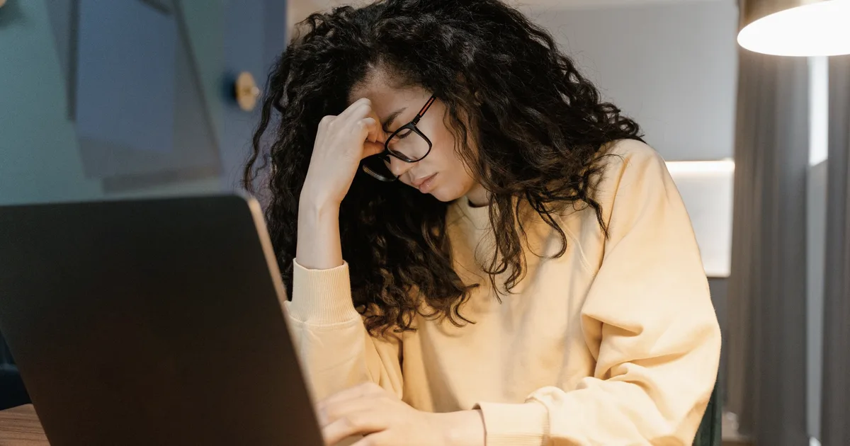 Femme fatiguée retirant ses lunettes devant son ordinateur portable