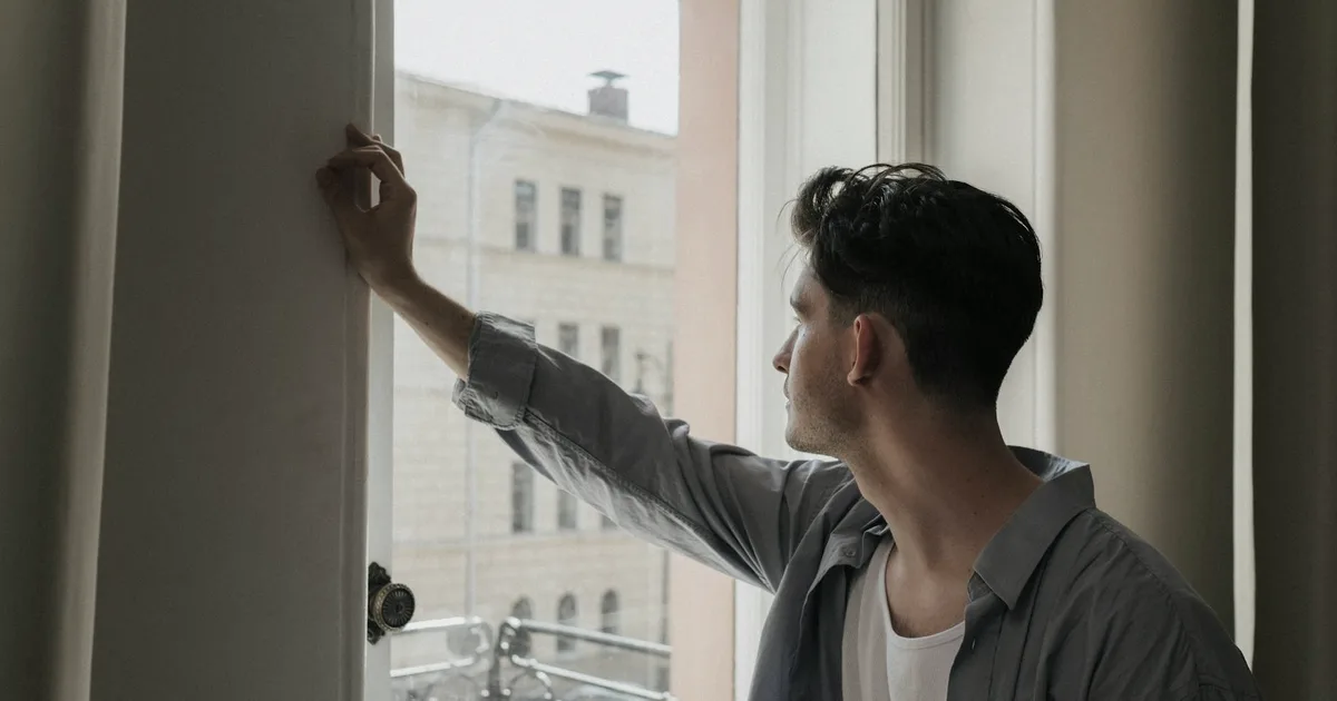 Pensive man leaning by a window in a bright room