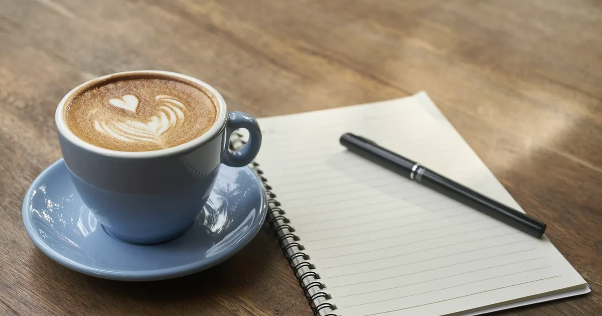 Tasse de café posée à côté d'un carnet ouvert sur une table en bois