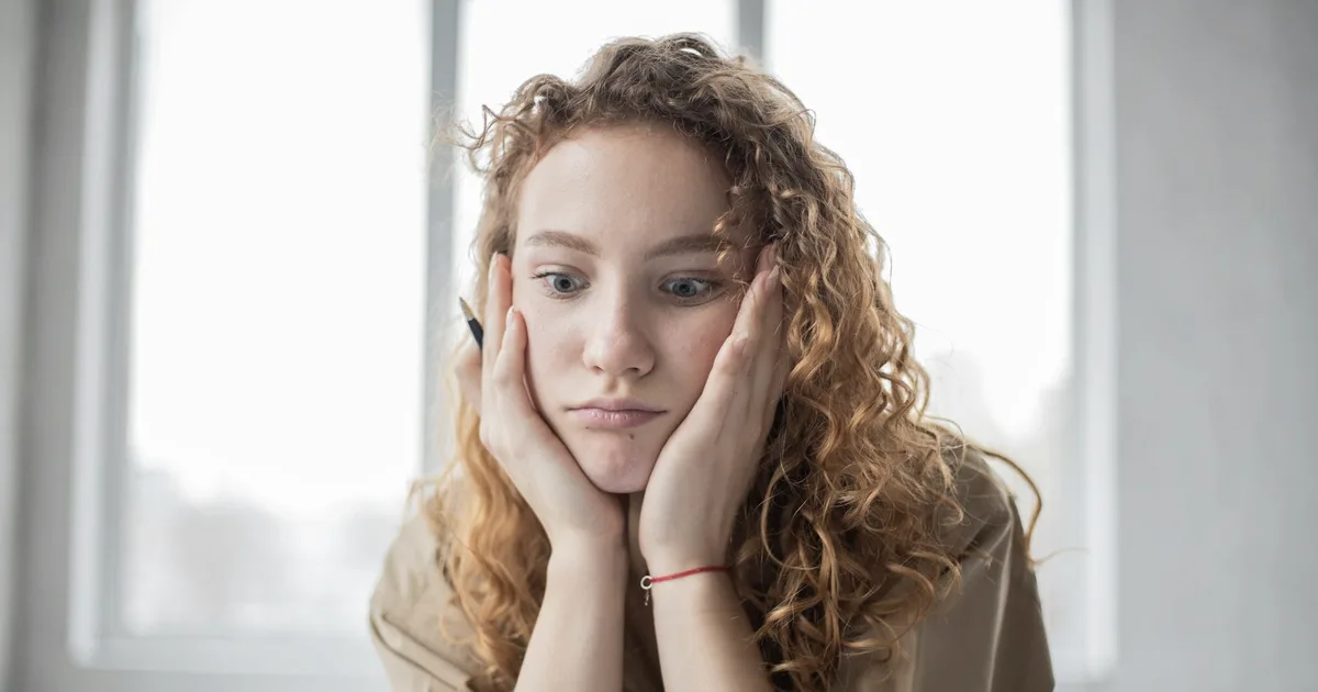 Young woman with her head in her hands, holding a pen, staring blankly