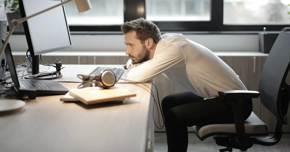 Man slumped over his desk, head on his arm, in front of a blank screen