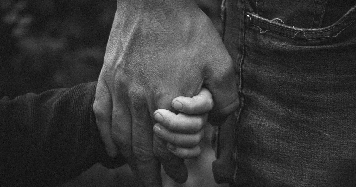 Adult's hand holding a child's hand, black and white photograph, close-up on the fingers