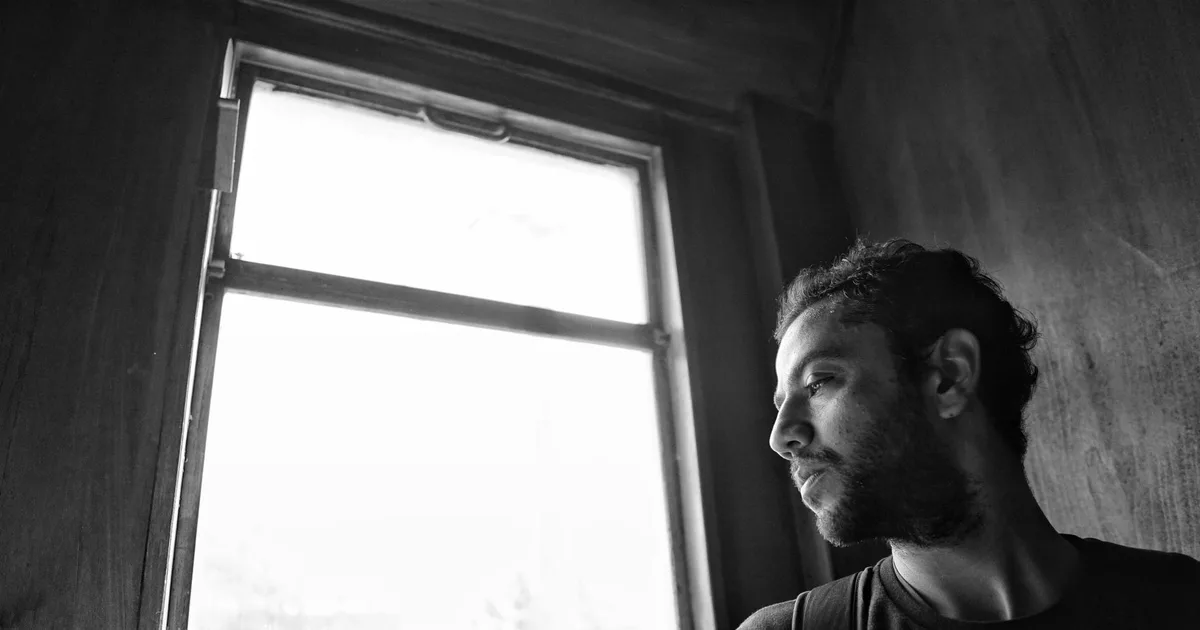 Bearded man in profile looking out a window, black and white photograph, contemplative mood
