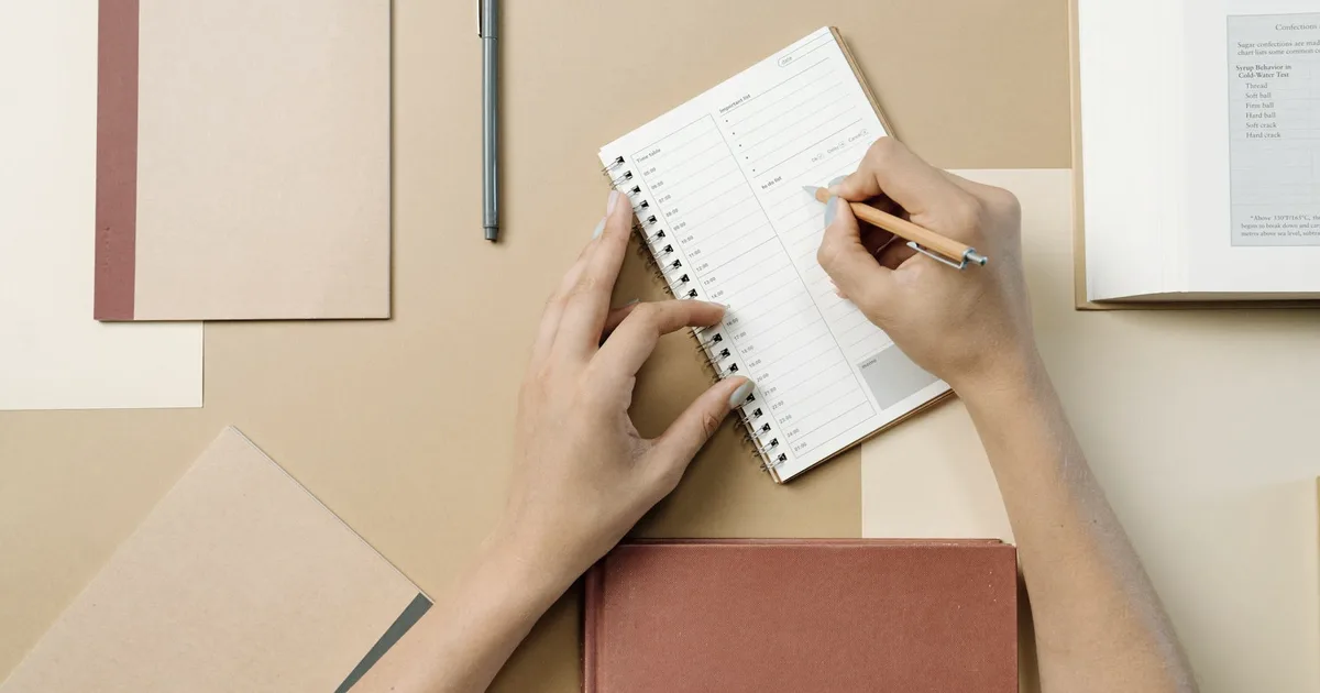 Top view of hands filling out a paper planner with a pen