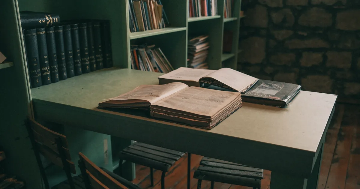 Old books open on a table in a library with dark green shelves