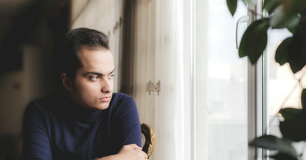 A pensive man looking out a window in a quiet room