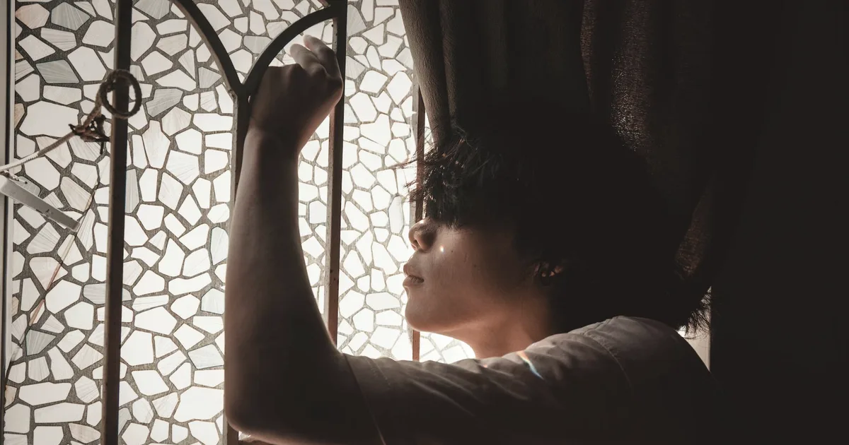 A tense person beside a window in soft light