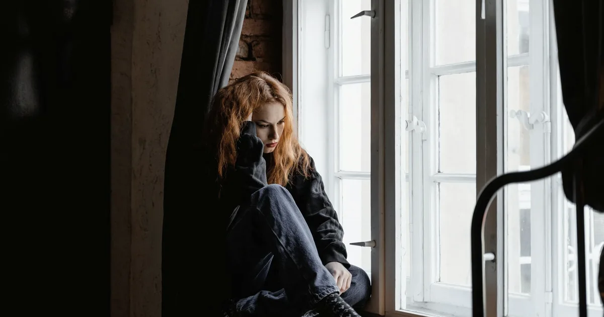 A person curled up by a window, lost in thought