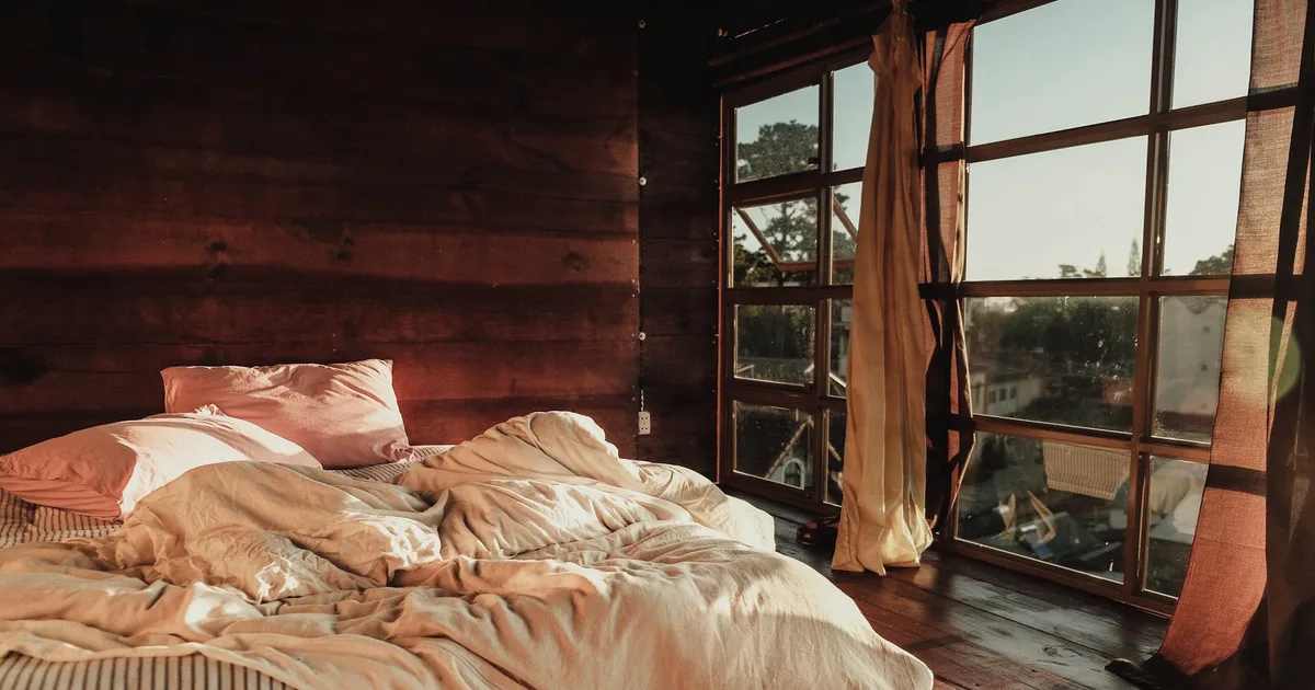 An unmade bed in a room filled with warm morning light