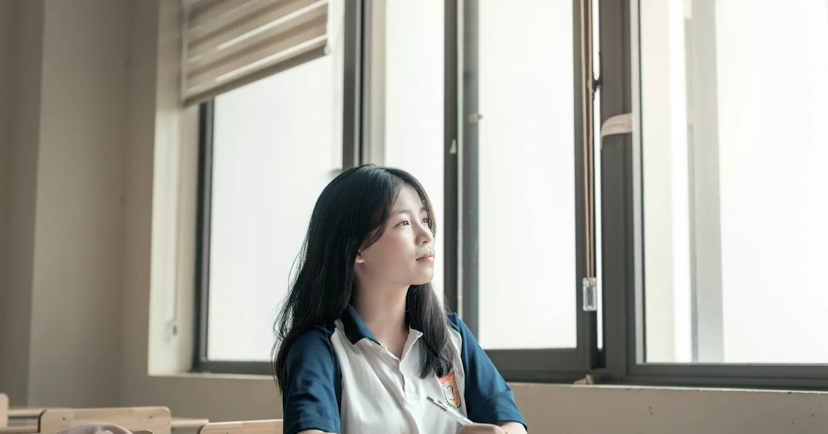 A child sitting in a classroom, gazing out the window, lost in thought