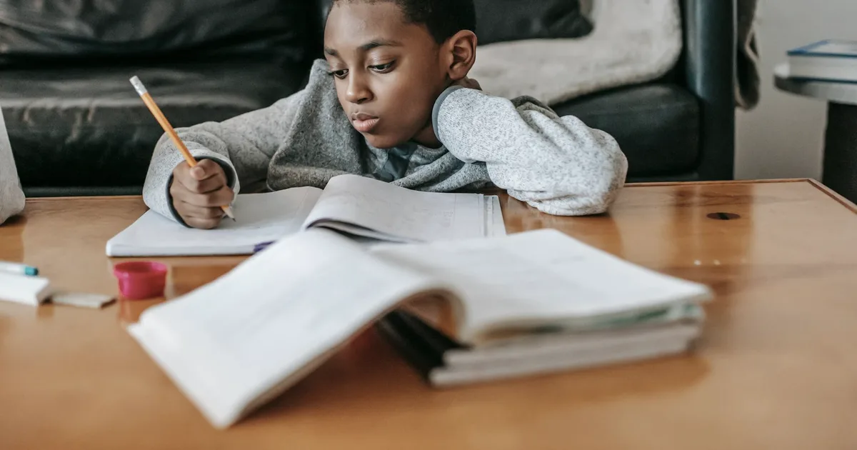 A young boy focused on his homework at a wooden table