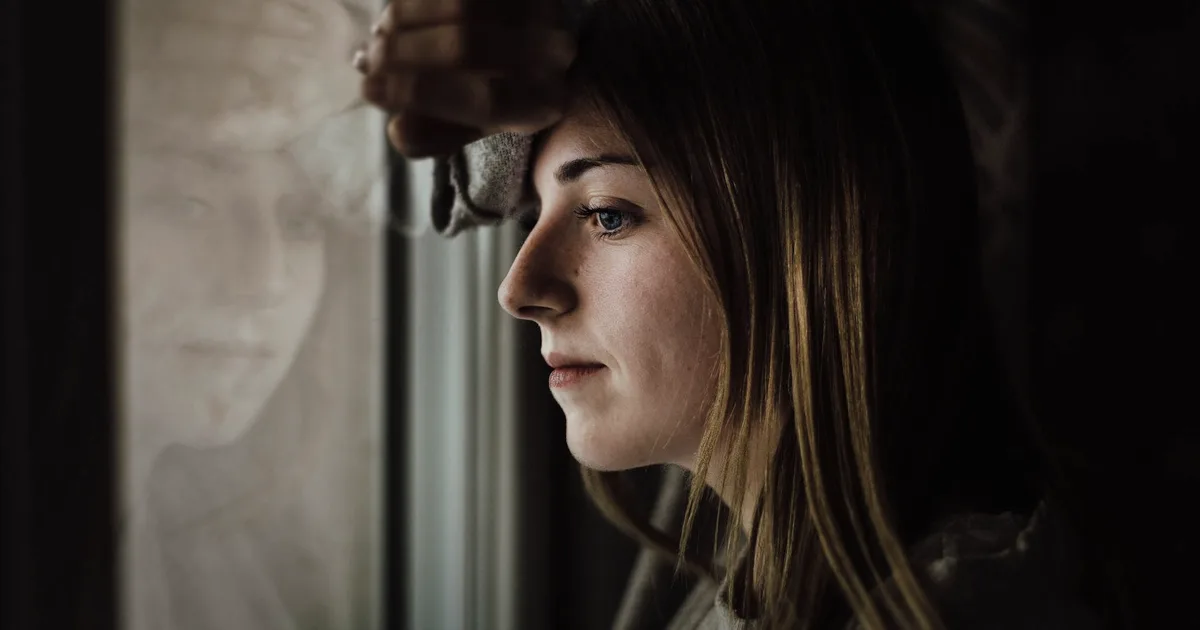 Adult woman leaning thoughtfully against a window in soft light