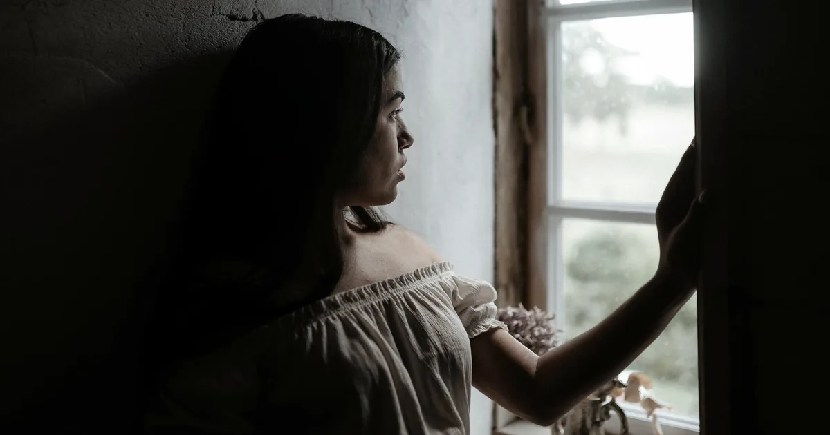 Adult woman alone by a window, looking out