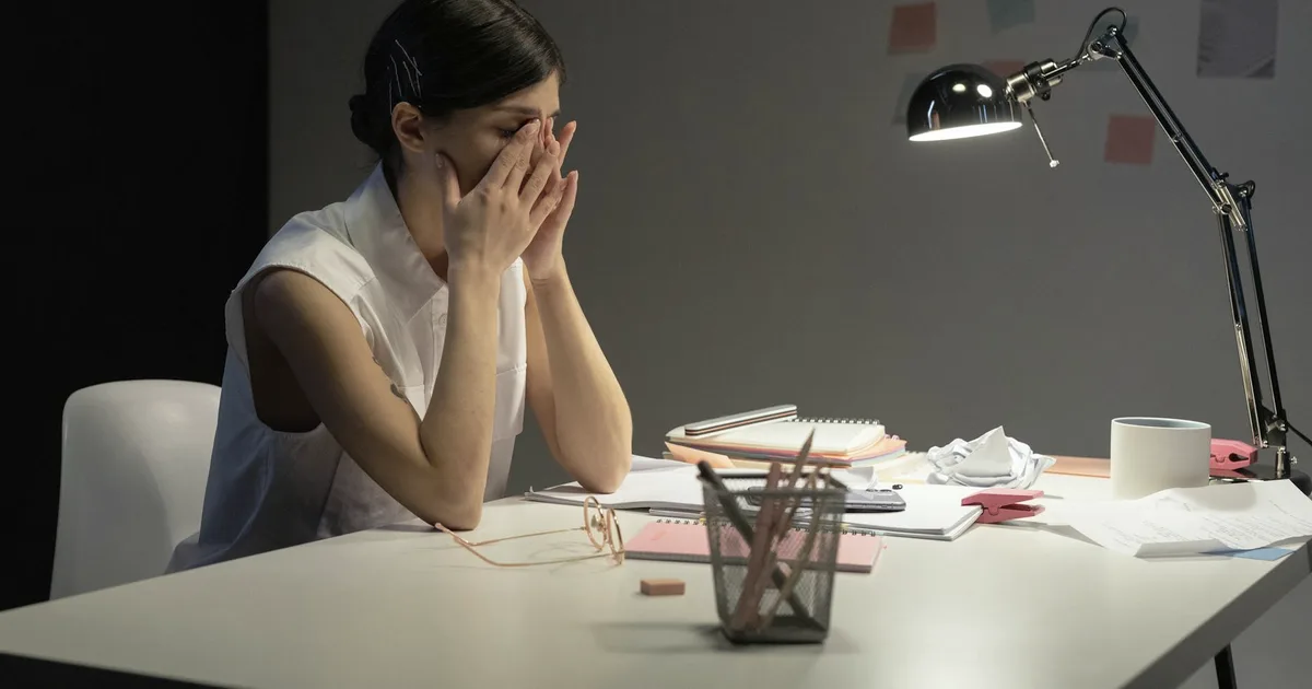 Overwhelmed woman at a cluttered desk with her face in her hands, an image of adult ADHD symptoms