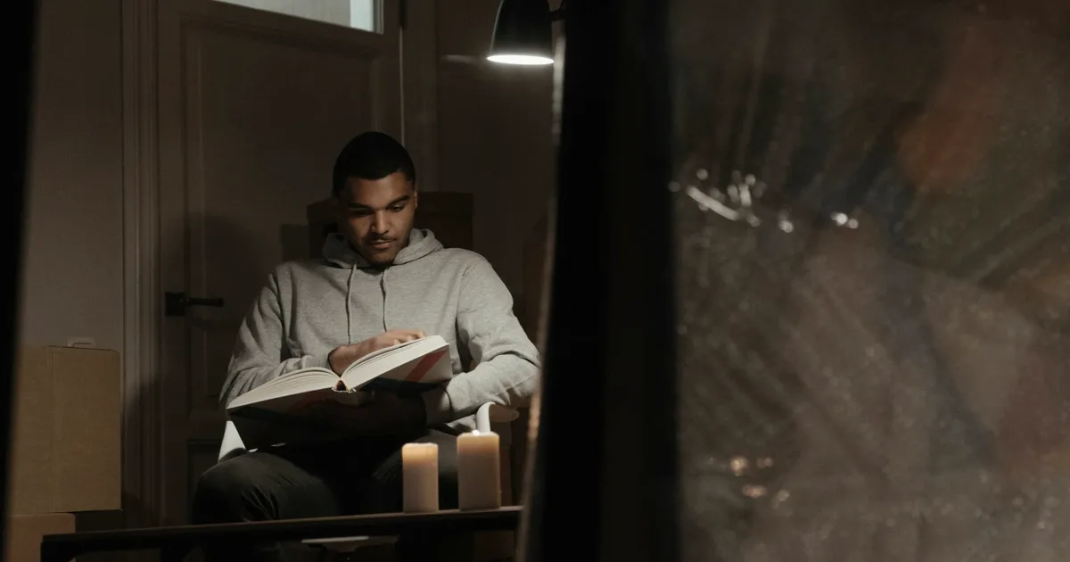 A person reading a book under the warm glow of a lamp